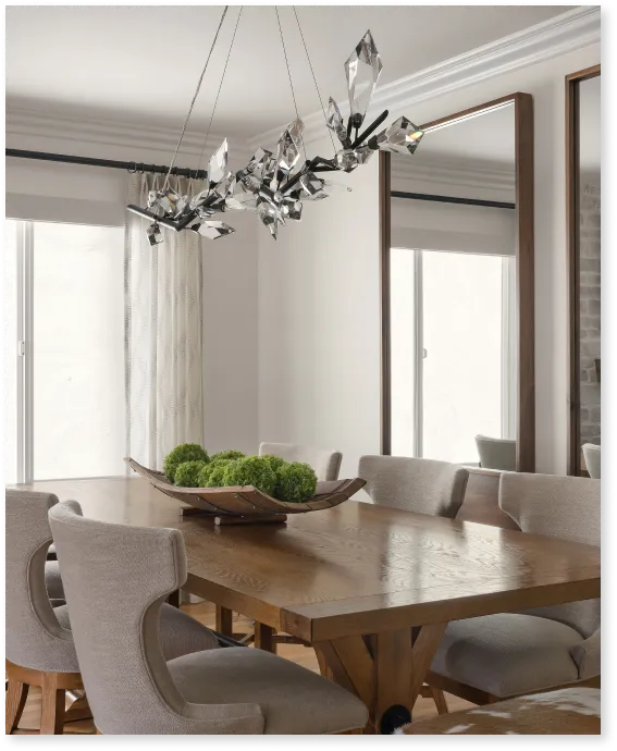Modern dining room with wooden table, upholstered chairs, decorative centerpiece, and crystal chandelier.